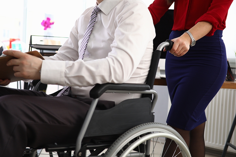 Female caregiver assisting a man in a wheelchair in a workplace setting, supporting mobility and accessibility