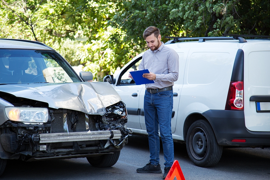 Insurance agent inspecting a damaged vehicle and writing notes on a clipboard for accident claim assessment