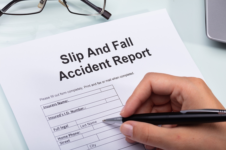 Woman filling out a slip and fall accident report form on a desk, documenting injury details for a claim