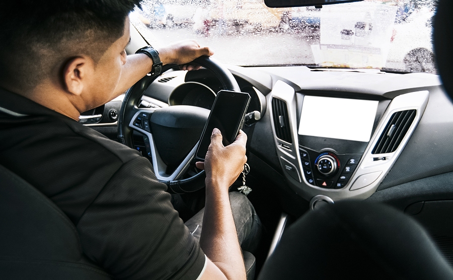 Driver texting on a mobile phone while driving, illustrating dangerous distracted driving behavior