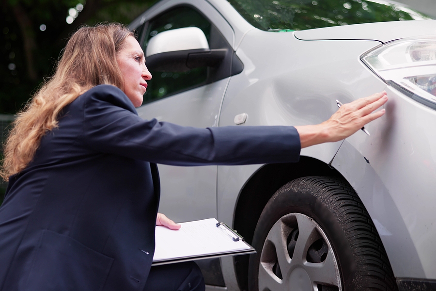 Car insurance adjuster inspecting vehicle damage and documenting details for claim assessment