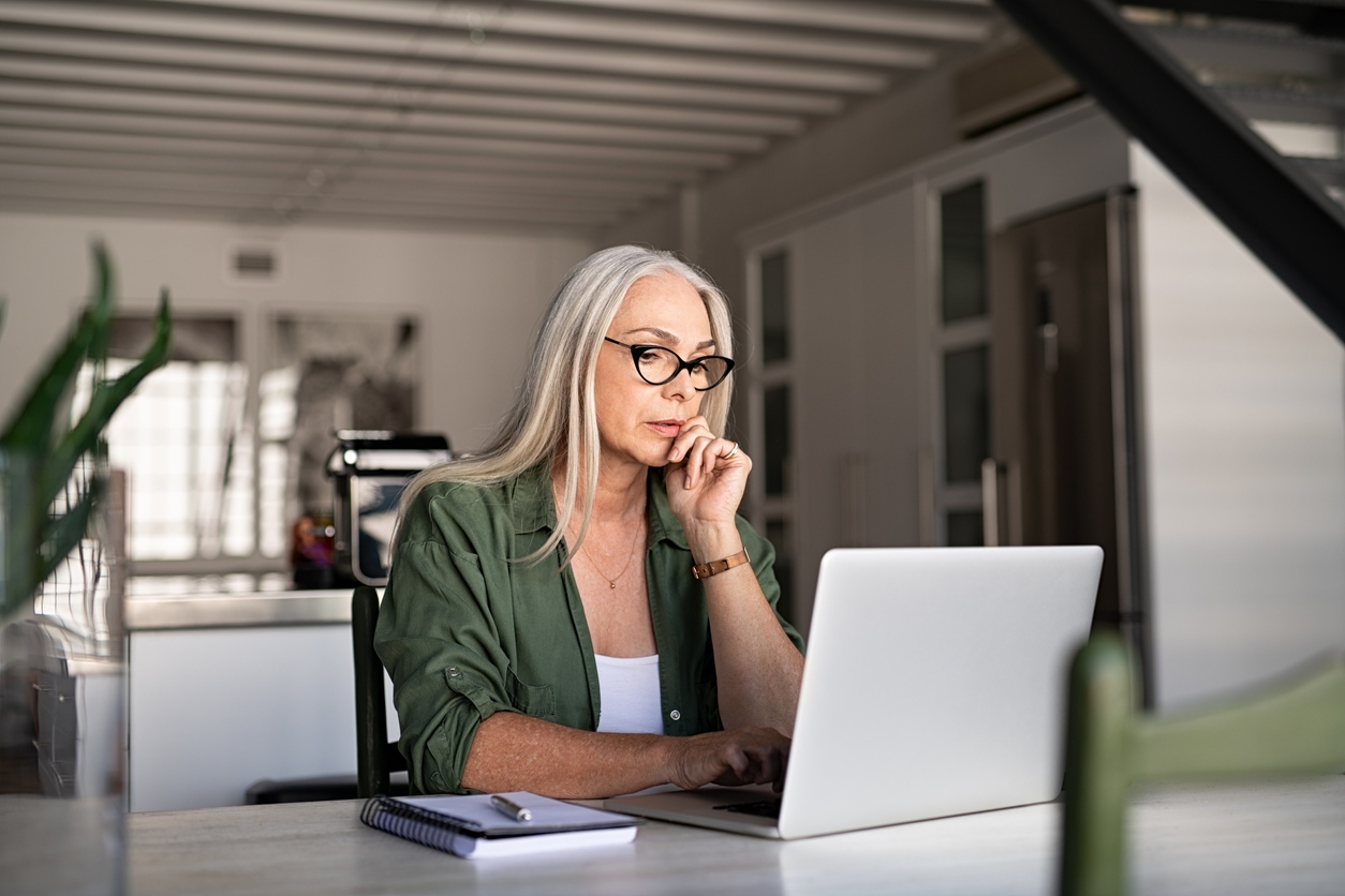 Worried senior woman using a laptop at home, looking stressed about finances or online tasks