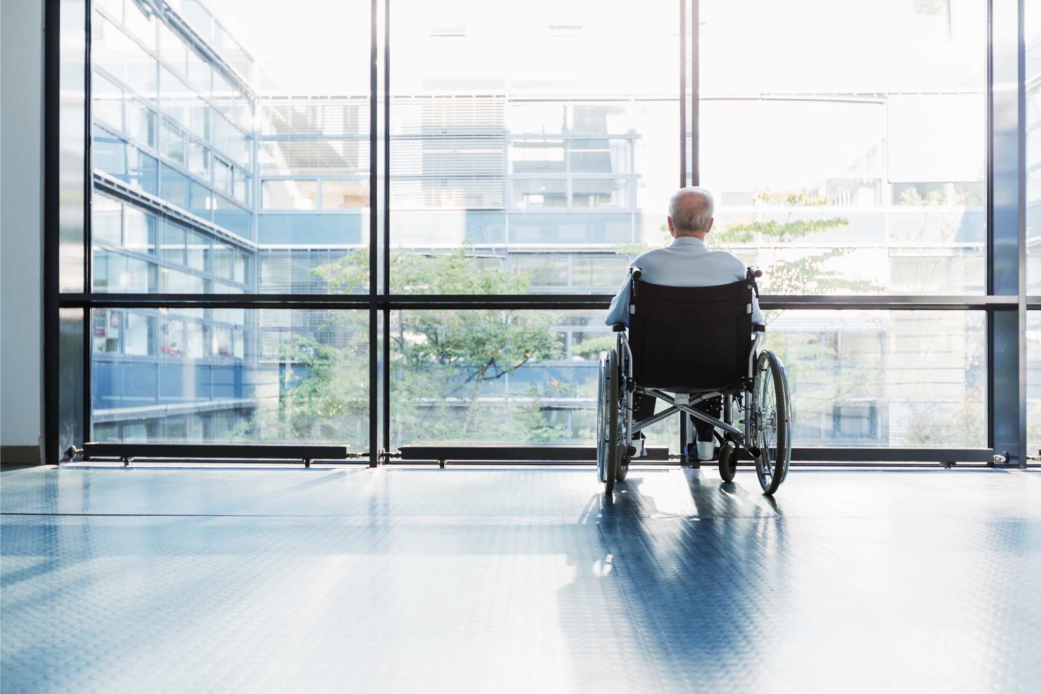 An older man in a wheelchair looks out a hospital window at the city skyline