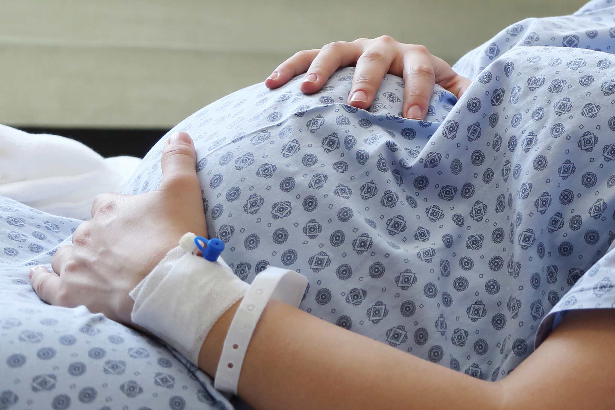 Pregnant woman lying in a hospital bed with hands resting on her belly and a hospital wristband on her arm.