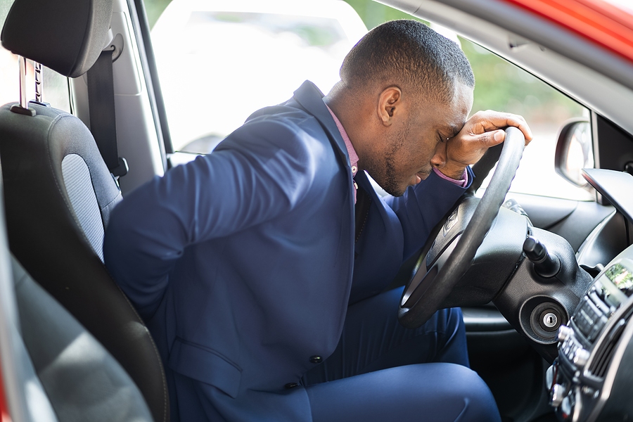 Driver experiencing severe back pain after a car accident, holding their lower back near a damaged vehicle