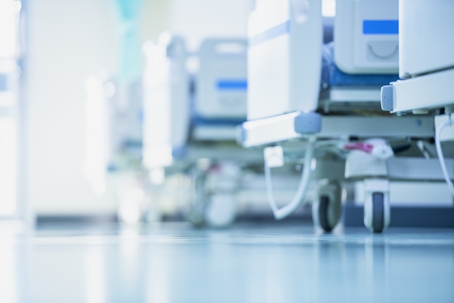 Empty hospital bed in clean clinic room with medical equipment ready for patient care