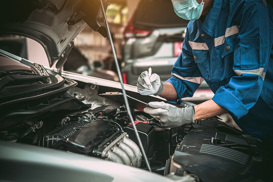 Car mechanic performing maintenance on a vehicle in a garage, checking engine components and ensuring proper functionality