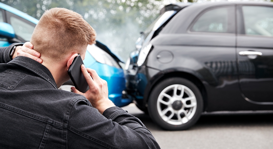 Young male driver involved in a car accident calling for roadside assistance or insurance support
